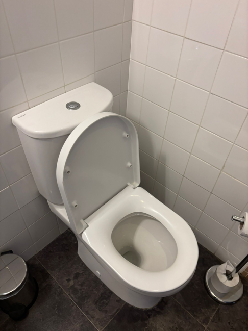 Close-coupled white toilet with cistern installed in tiled bathroom