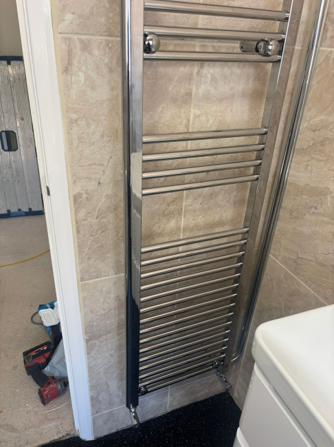 Chrome heated towel rail fitted in tiled bathroom