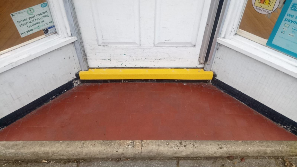 Yellow safety door threshold strip on tiled floor entrance