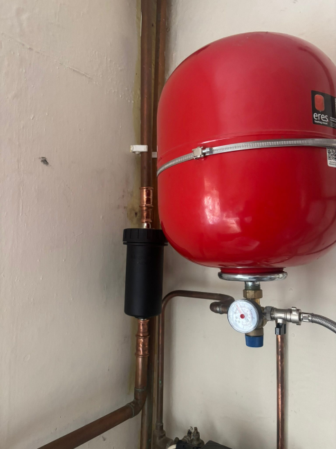 Red expansion vessel with copper pipework and pressure gauge